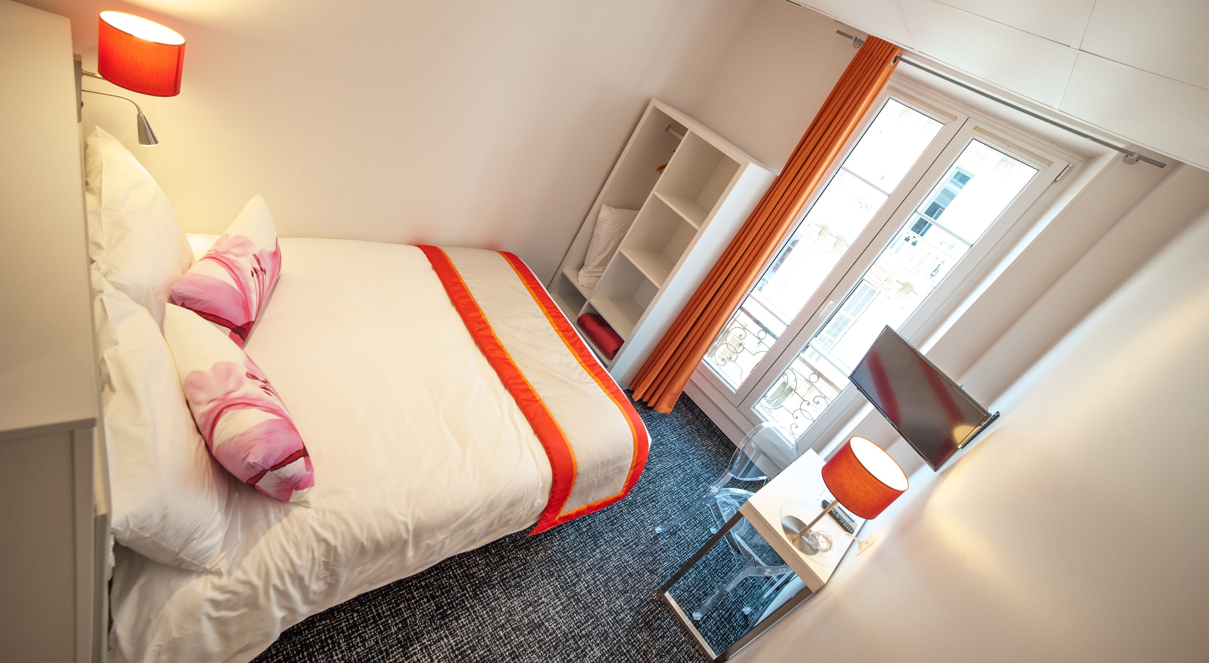 Une chambre d’hôtel comprenant un lit, une table de chevet, une lampe, une fenêtre avec des rideaux et une armoire.