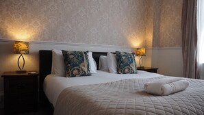 Una cama bien tendida con un edredón acolchado, dos lámparas de noche y almohadas estampadas.