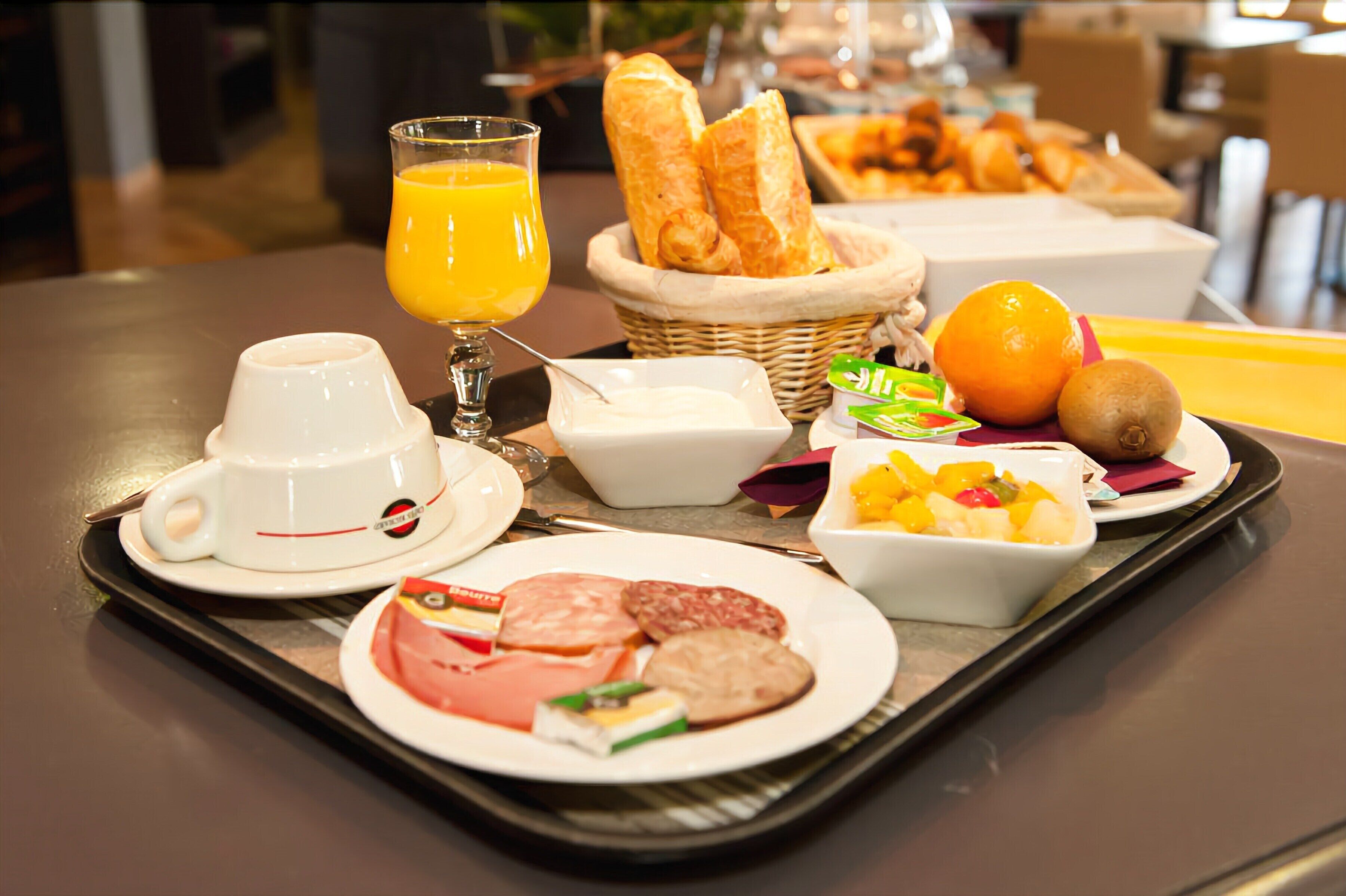 A breakfast tray with croissants, orange juice, yogurt, fruit, and various meats.