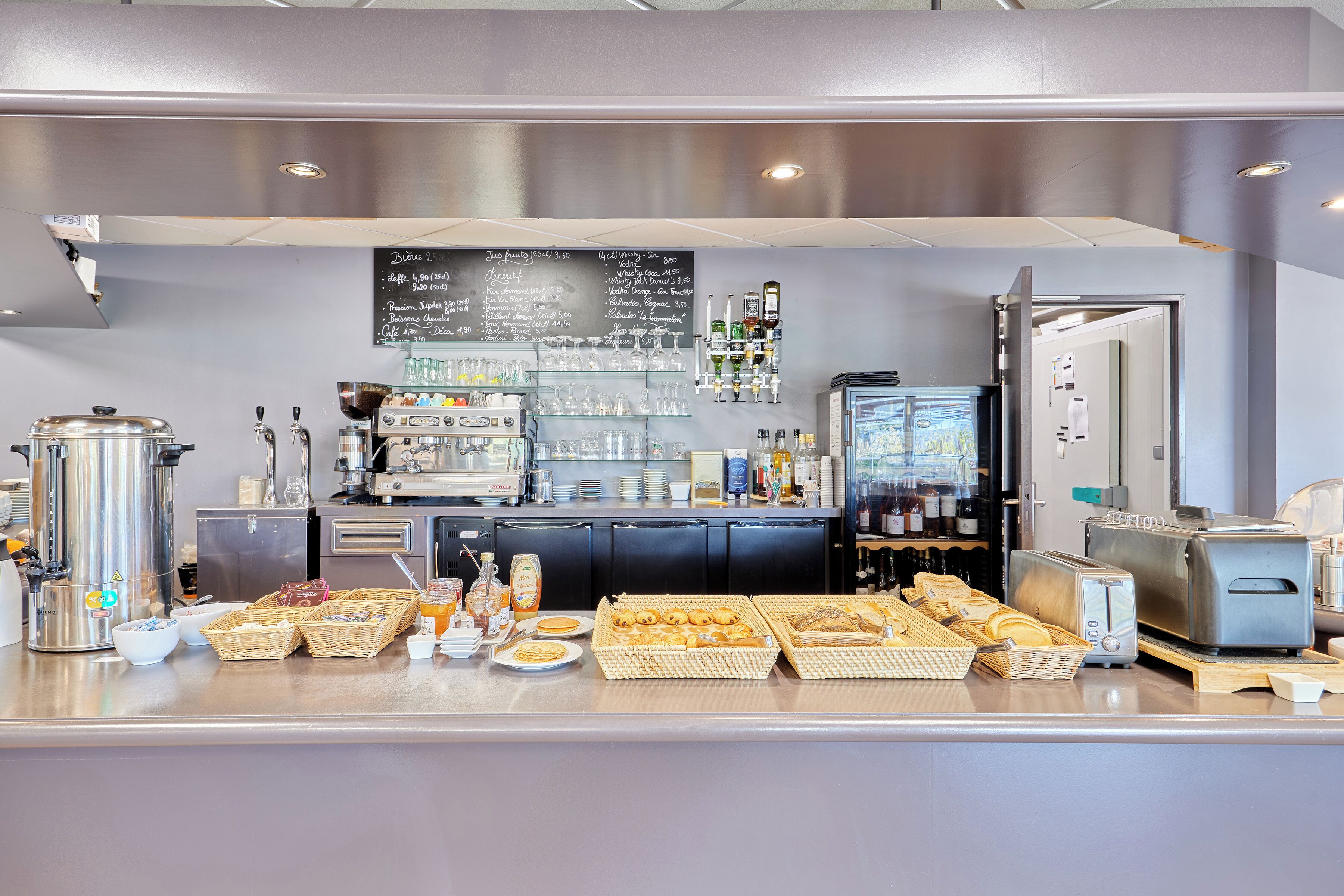 A commercial kitchen with stainless steel appliances, a chalkboard menu, and various food items displayed.