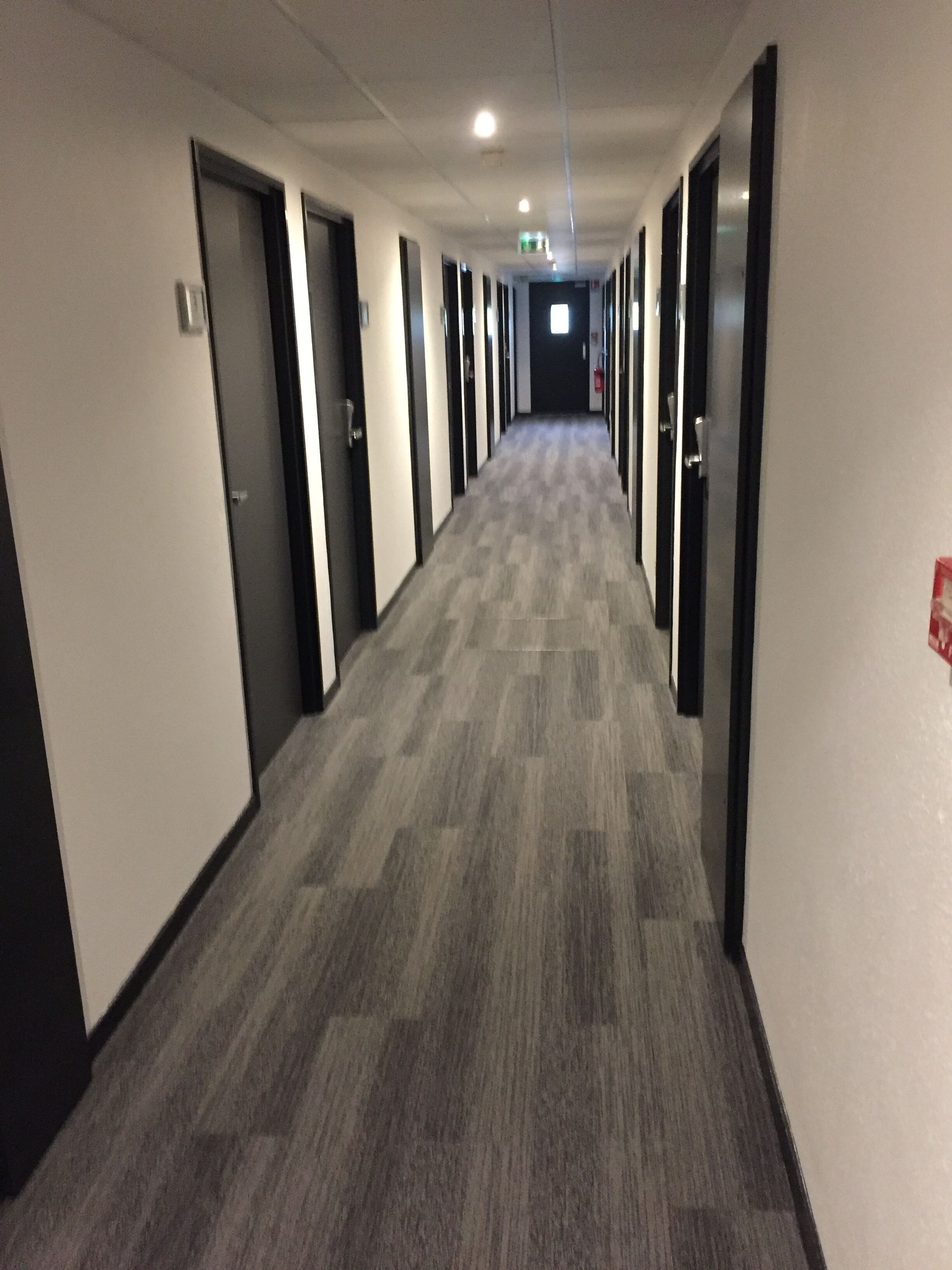 Un pasillo largo y estrecho con puertas a ambos lados, piso alfombrado e iluminación empotrada en el techo.
