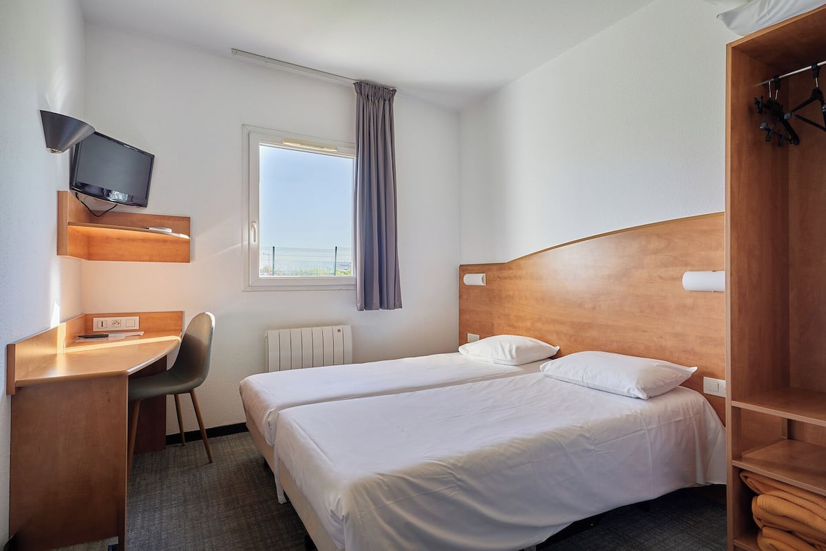 Ein Hotelzimmer mit zwei Betten, einem Schreibtisch, einem Stuhl, einem Fernseher und einem Fenster mit Vorhängen.