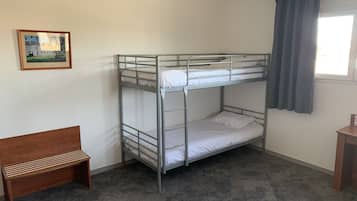 A bunk bed room with a wooden bench, carpeted floor, and a framed picture on the wall.
