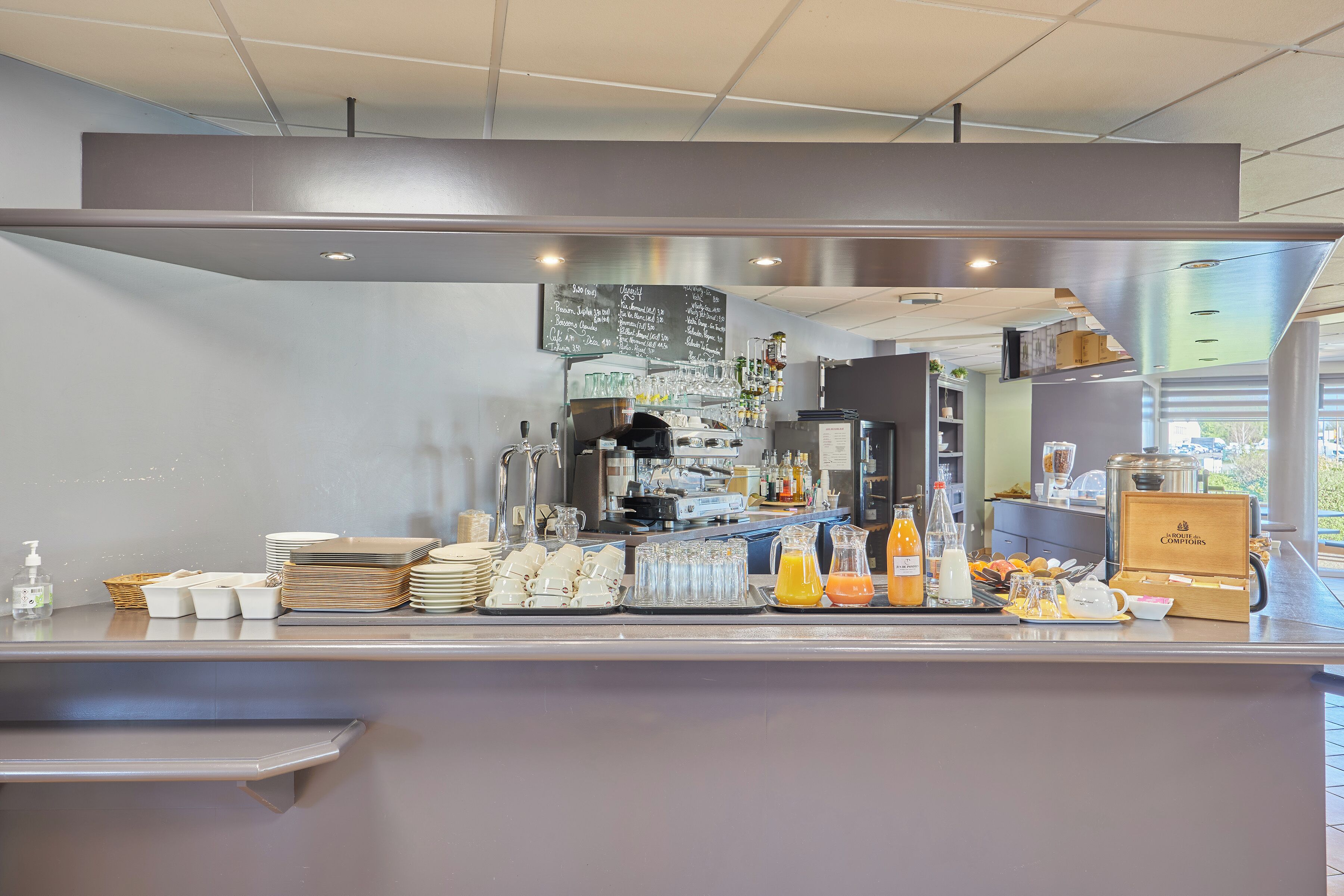 Un espace cuisine moderne doté d’un tableau noir servant de menu, d’appareils électroménagers en acier inoxydable et d’une variété de produits alimentaires et de boissons disposés sur le comptoir.