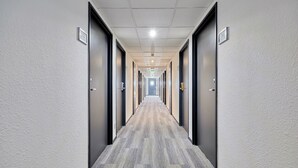A long, narrow hallway with doors on both sides, numbered signs above each door, and a carpeted floor. - Citotel Armony Hotel (Bourg-Achard)