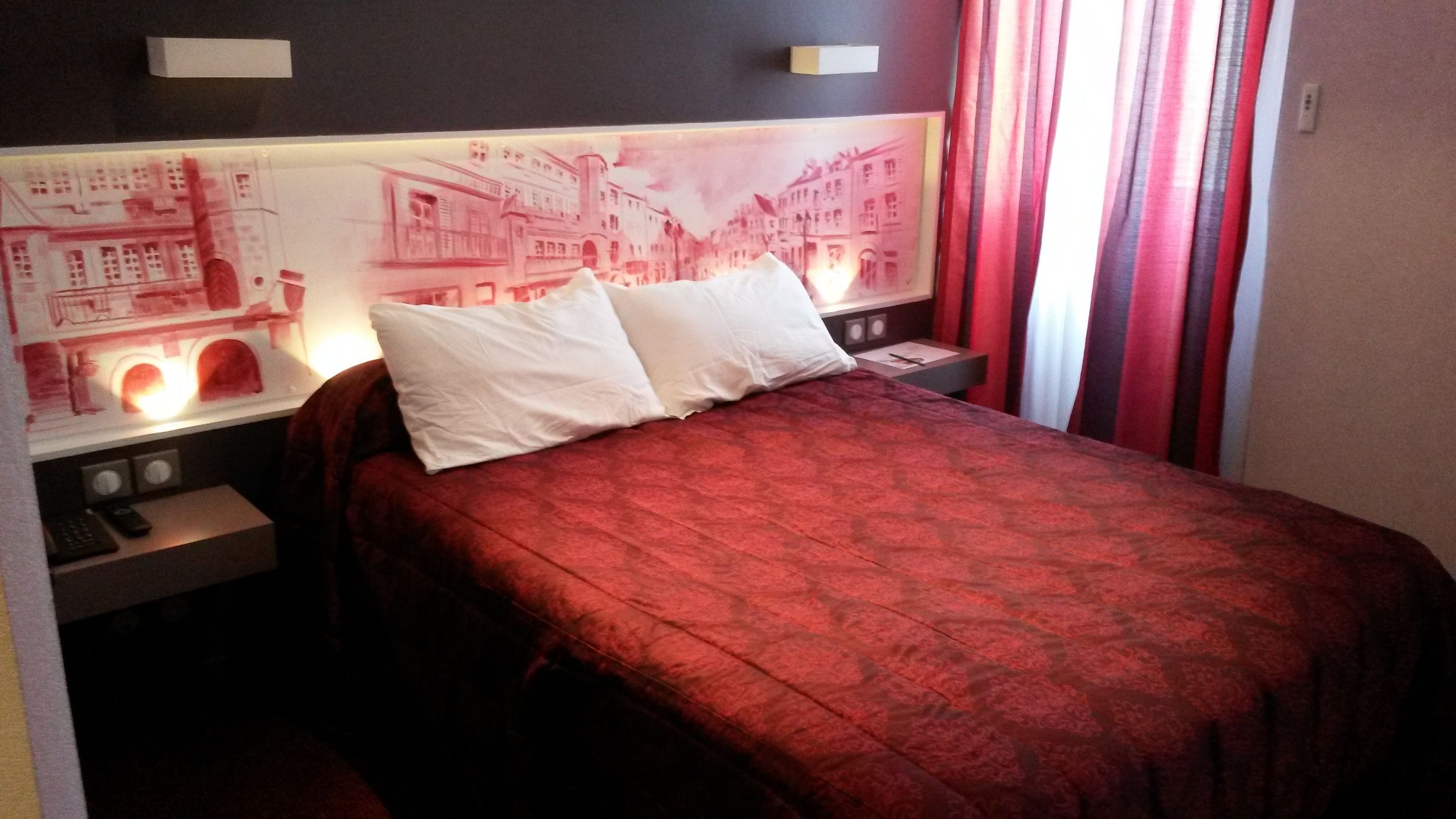 Una habitación de hotel con una cama, dos mesitas de noche y una lámpara fijada a la pared.