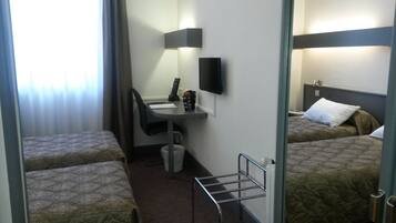 A hotel room with two single beds, a desk with a chair, a small table, a TV, and a window with curtains.