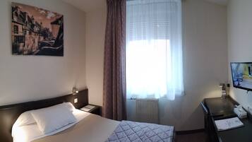 A hotel room with a bed, a desk, a TV, a painting, and a window with curtains.