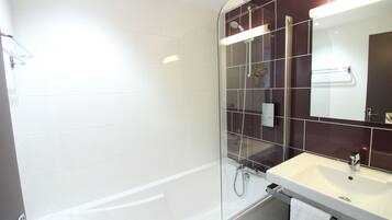 A modern bathroom with a glass-enclosed shower, a white bathtub, and a vanity with a mirror.