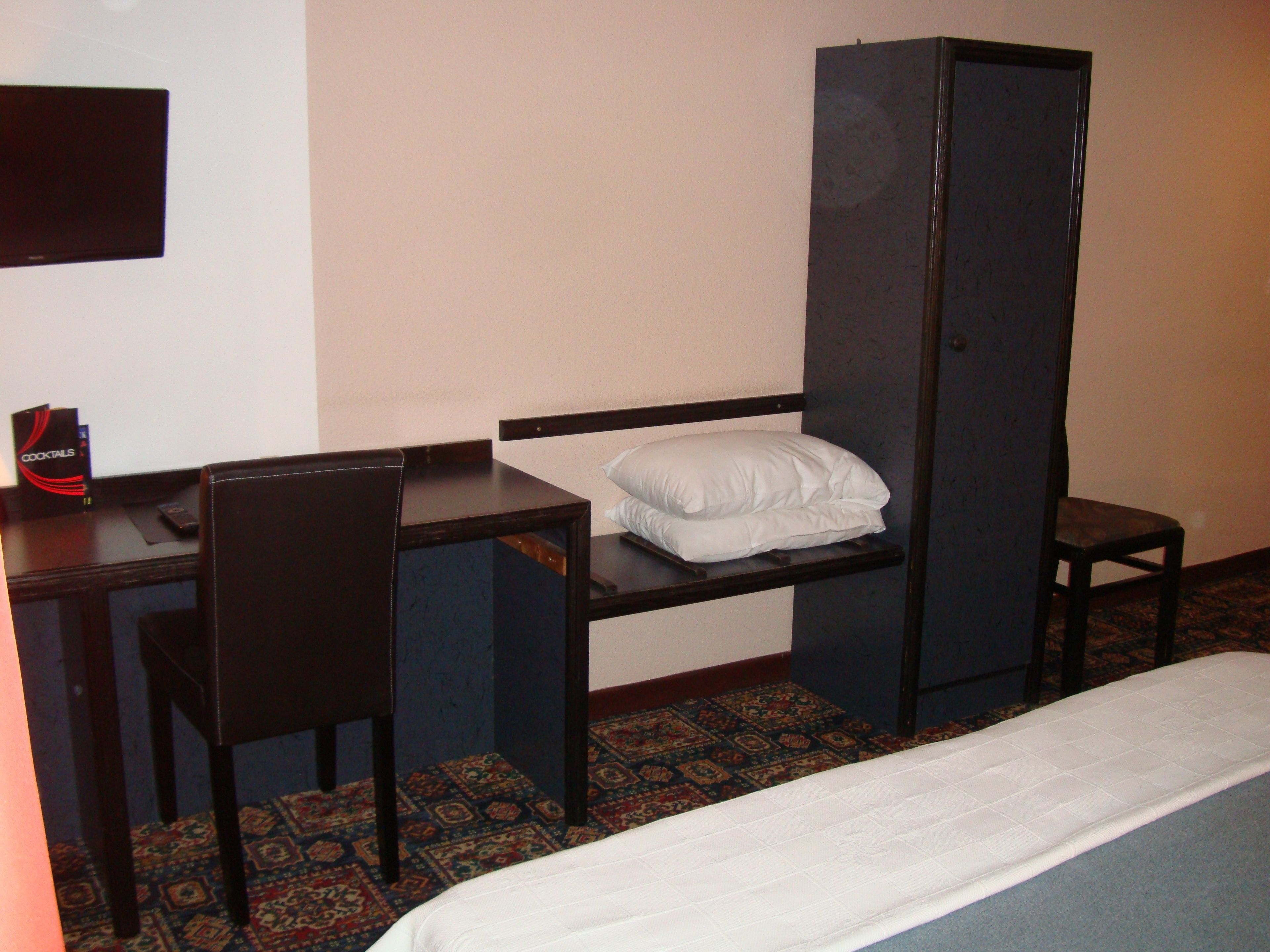 Habitación de hotel con una cama individual, un escritorio con silla, un armario y una mesita con un menú.