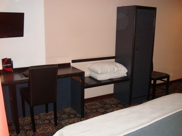 Habitación de hotel con una cama individual, un escritorio con silla, un armario y una mesita con un menú.