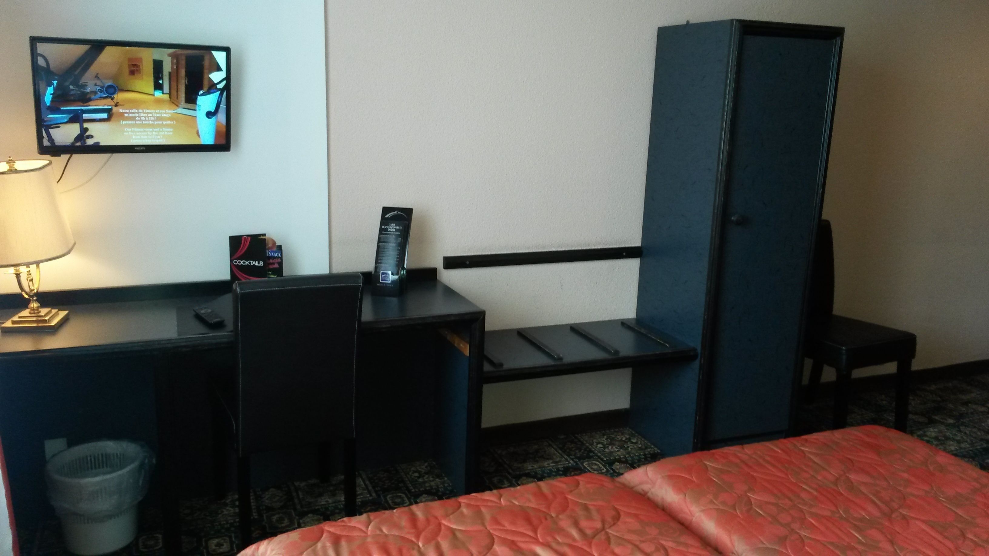 Quarto de hotel com uma cama, uma escrivaninha com computador, televisão, lixeira e minibar.