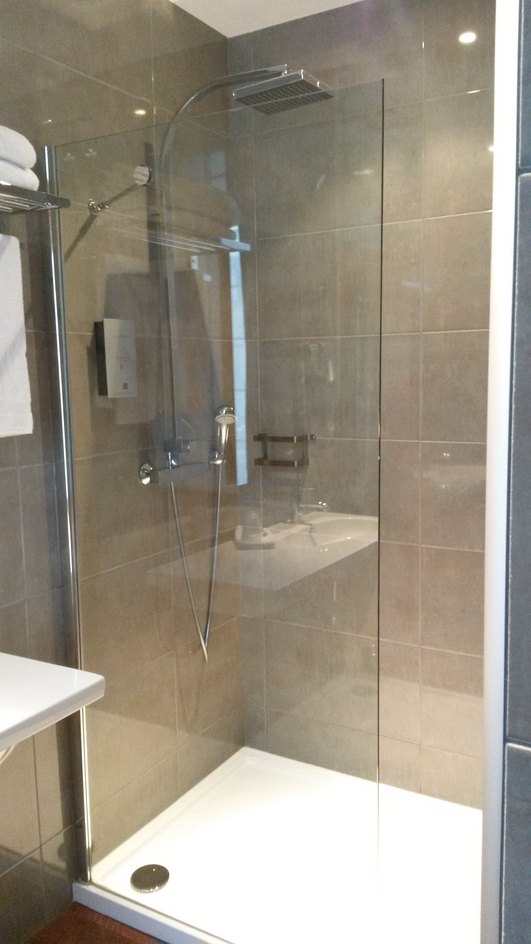 Una ducha moderna con mampara de vidrio, cabezal de ducha de mano y panel de control en la pared.
