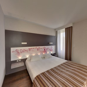 Una habitación de hotel moderna con una cama grande, cabecera con una obra de arte de paisaje urbano, mesitas de noche con lámparas y una ventana con cortinas.