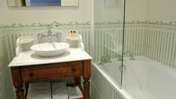 A bathroom with a white sink, mirror, and bathtub. There are two bottles on the sink and a towel rack below it.