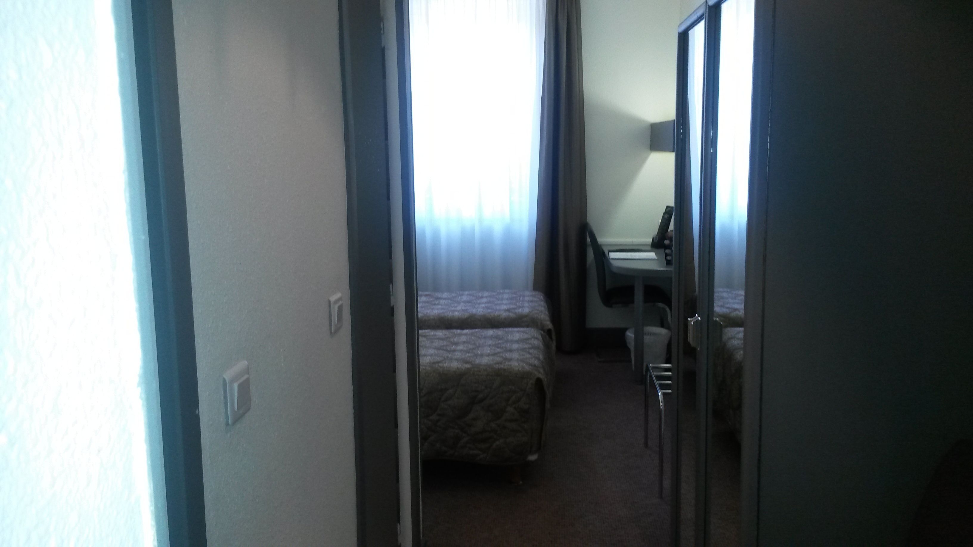 Ein schmaler Flur, der zu einem Schlafzimmer mit Bett und Schreibtisch führt.