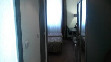 Ein schmaler Flur, der zu einem Schlafzimmer mit Bett und Schreibtisch führt.