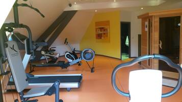 A gym with various exercise equipment, including treadmills and stationary bikes, in a room with a sloped ceiling and wooden walls.