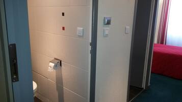 Casa de banho com sanita, dispensador de papel e secador de mãos.