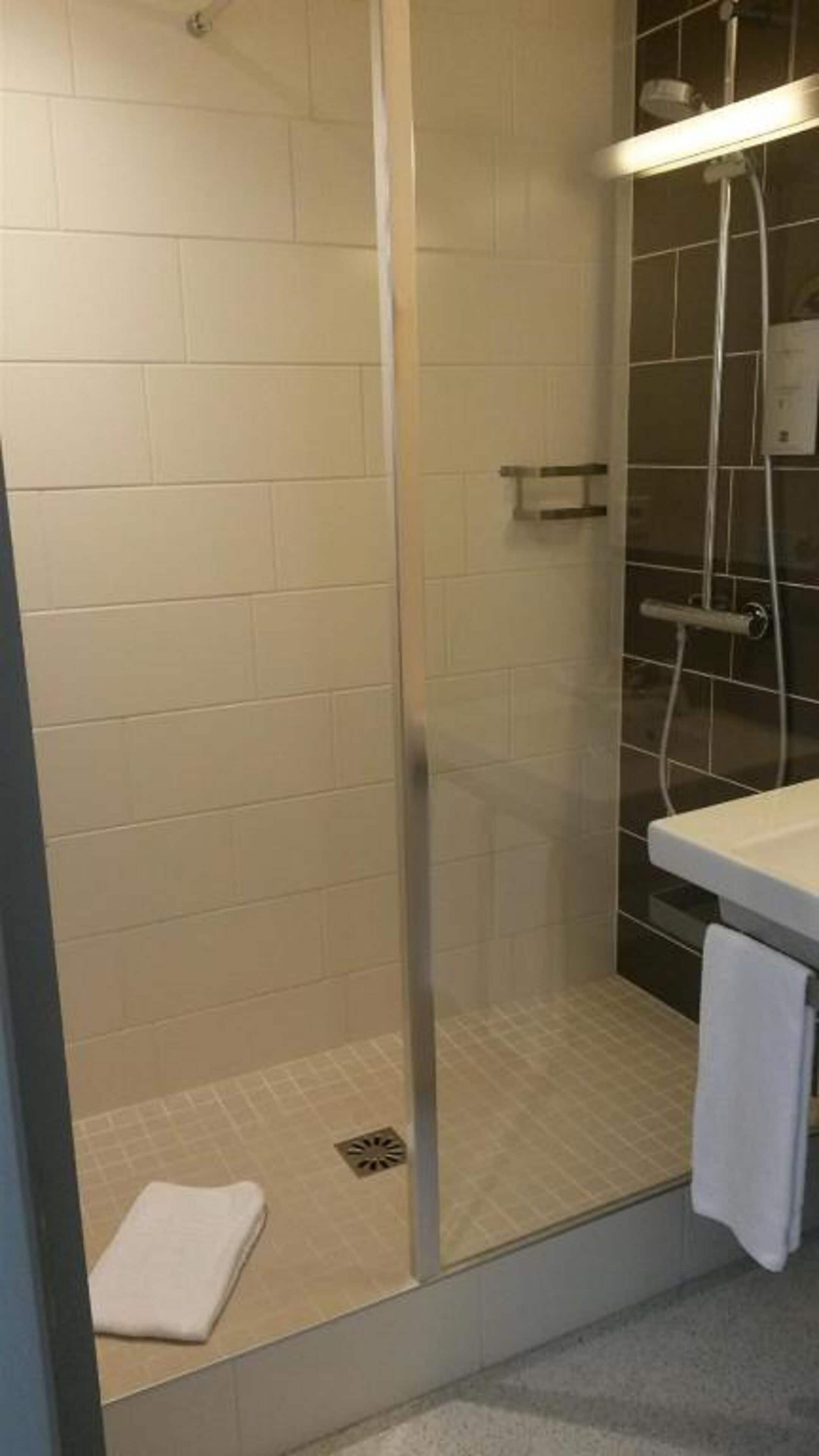 A shower with a glass door, a white towel on the floor, and a towel hanging on a rack.