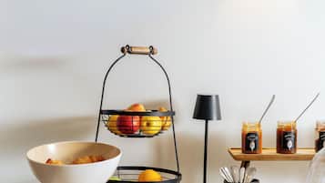 Une table blanche dressée pour le petit-déjeuner, avec un panier de fruits, un bol de croissants et une assiette de nourriture.