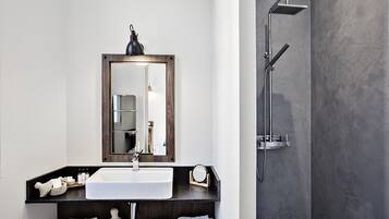 Un baño moderno con un lavabo blanco, encimera oscura y un espejo grande.