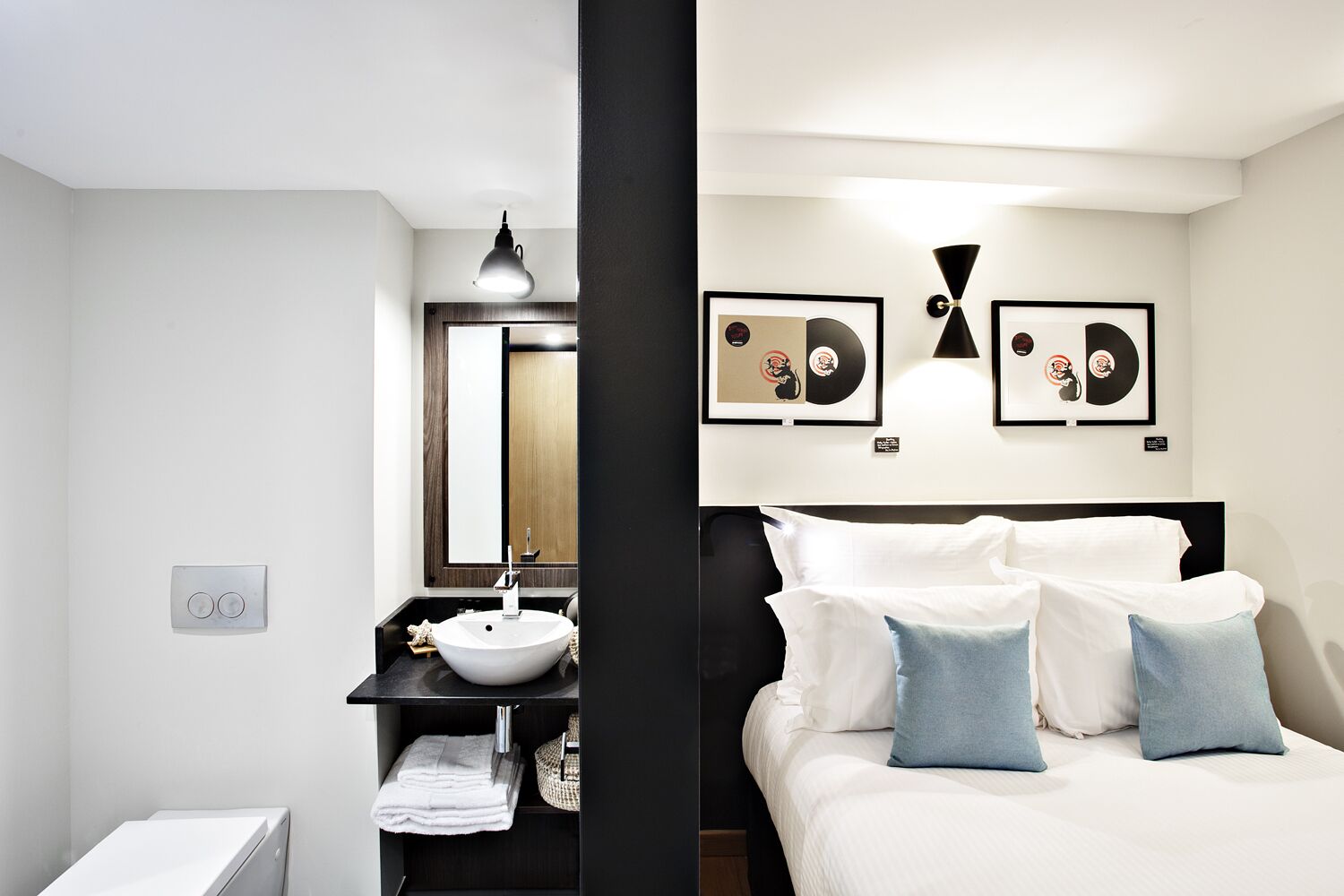 Una habitación de hotel moderna con una cama, una mesita de noche, un lavamanos y un espejo.