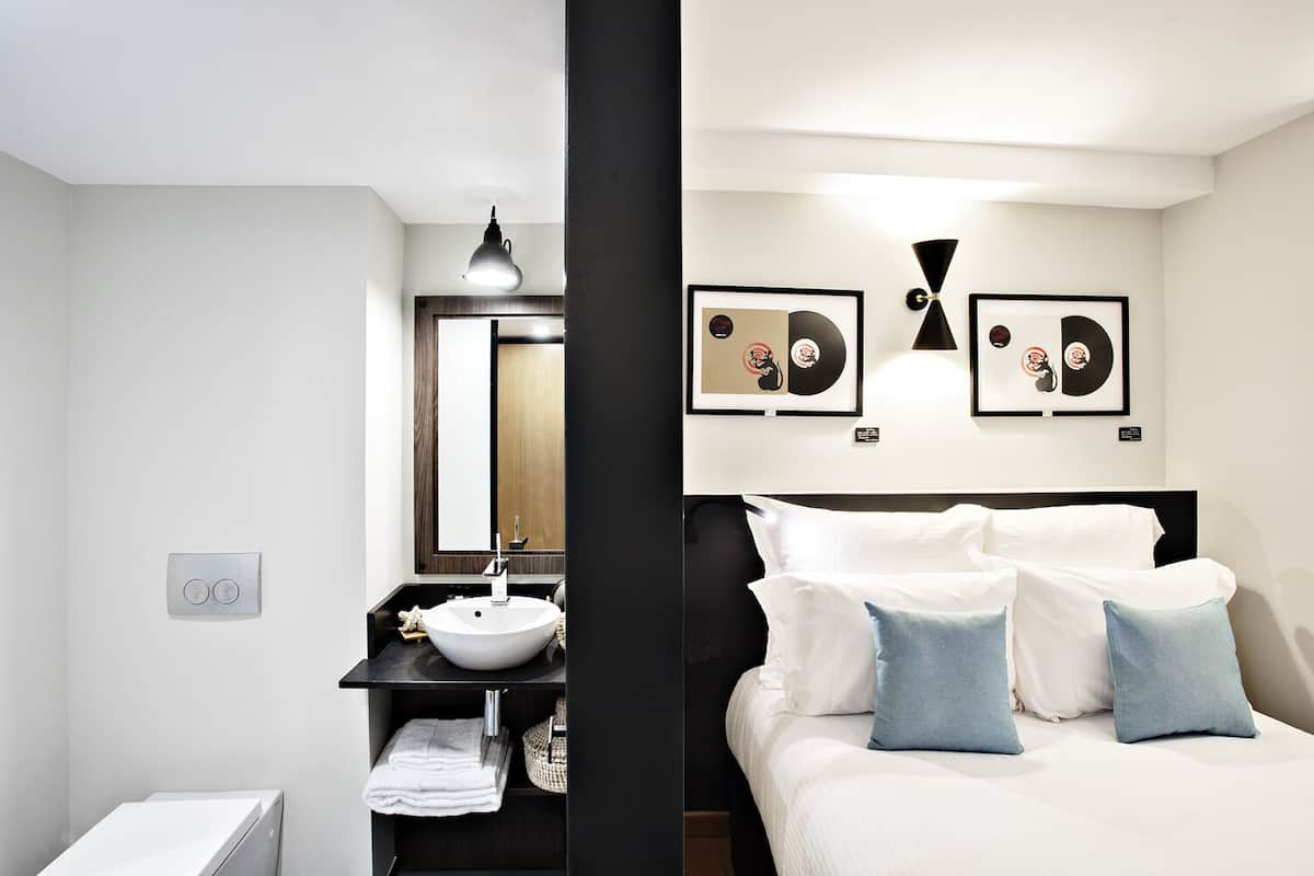 A modern hotel room with a bed, a bedside table, a sink, and a mirror.