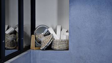 A corner of a room with a blue wall, a wooden shelf, and a woven basket containing white objects.
