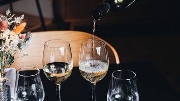 A dining table with a white plate of food, three wine glasses, and a bottle of wine being poured.