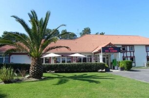 Un hotel con techo de tejas rojas, un cartel y un césped bien cuidado con una palmera.