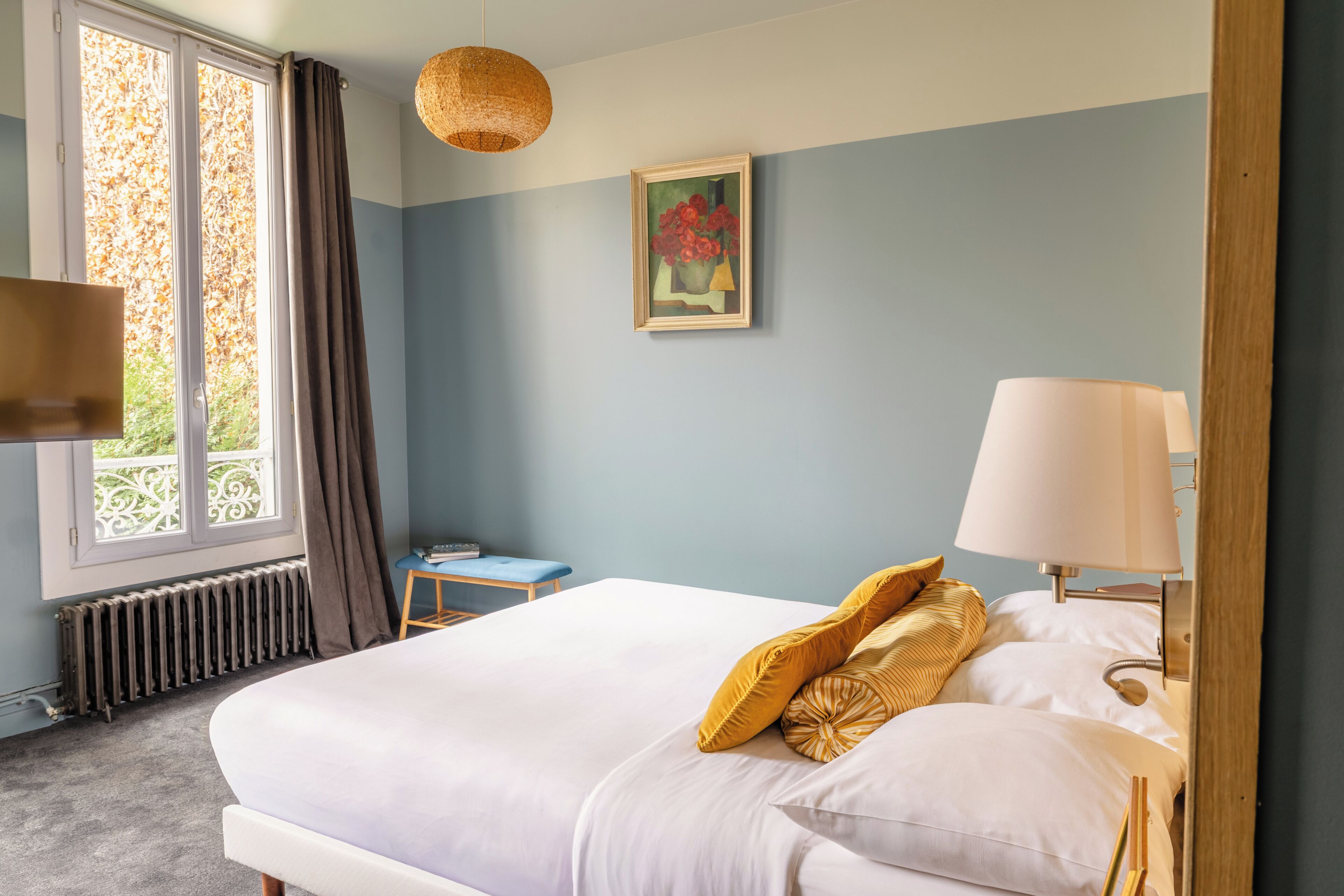 A bedroom with a bed, a bedside table, a lamp, a painting, and a window with curtains.