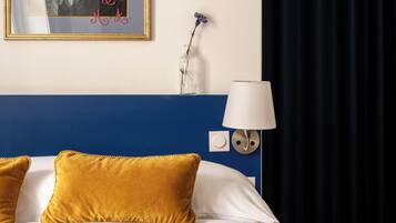 A hotel room with a large bed, a framed portrait, a lamp, and a dark curtain.
