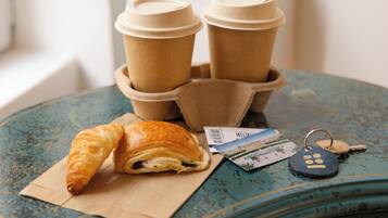 Ein blauer Tisch mit einem Croissant, zwei Kaffeetassen, einem Schlüsselanhänger und einer Postkarte.