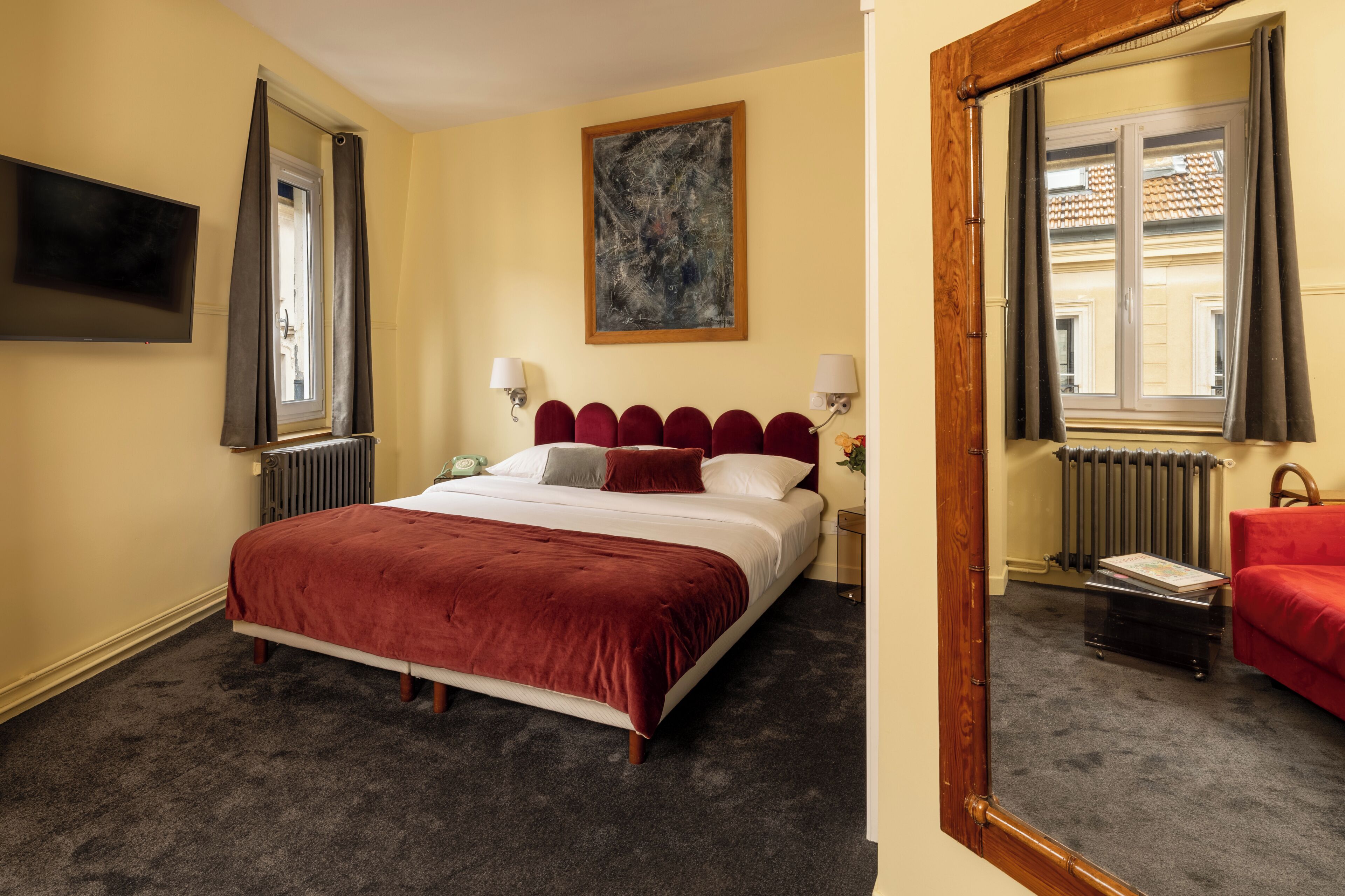 A hotel room with a large bed, a television, a painting, and a window with curtains.