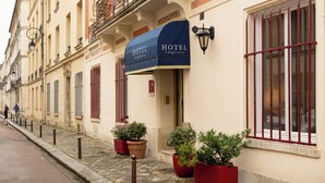 A hotel facade with a blue awning, potted plants, and a cobblestone street. - Hôtel d'Angleterre (Versailles)