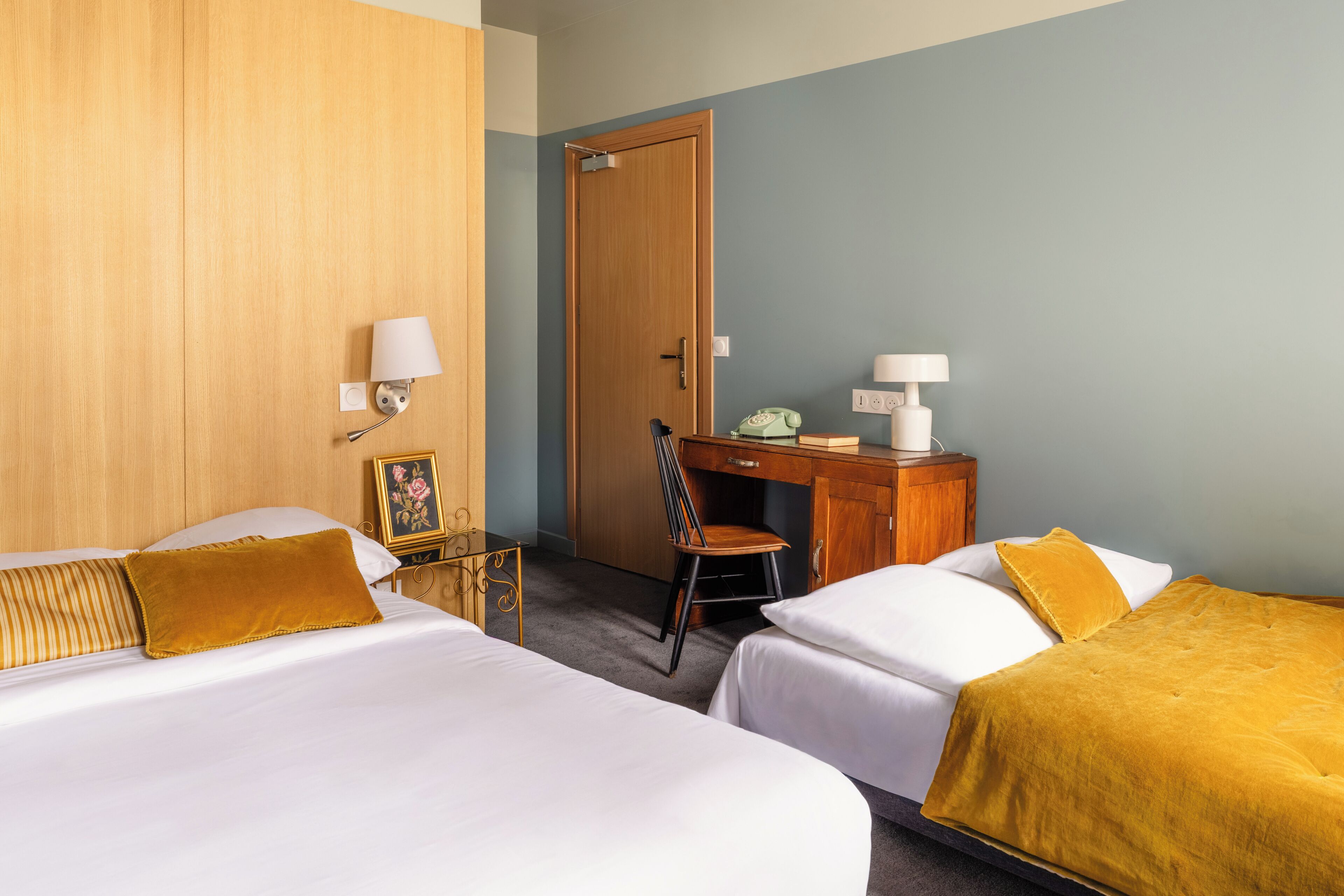 Une chambre d’hôtel avec deux lits, un bureau, une chaise, une armoire et une table de chevet avec une lampe.
