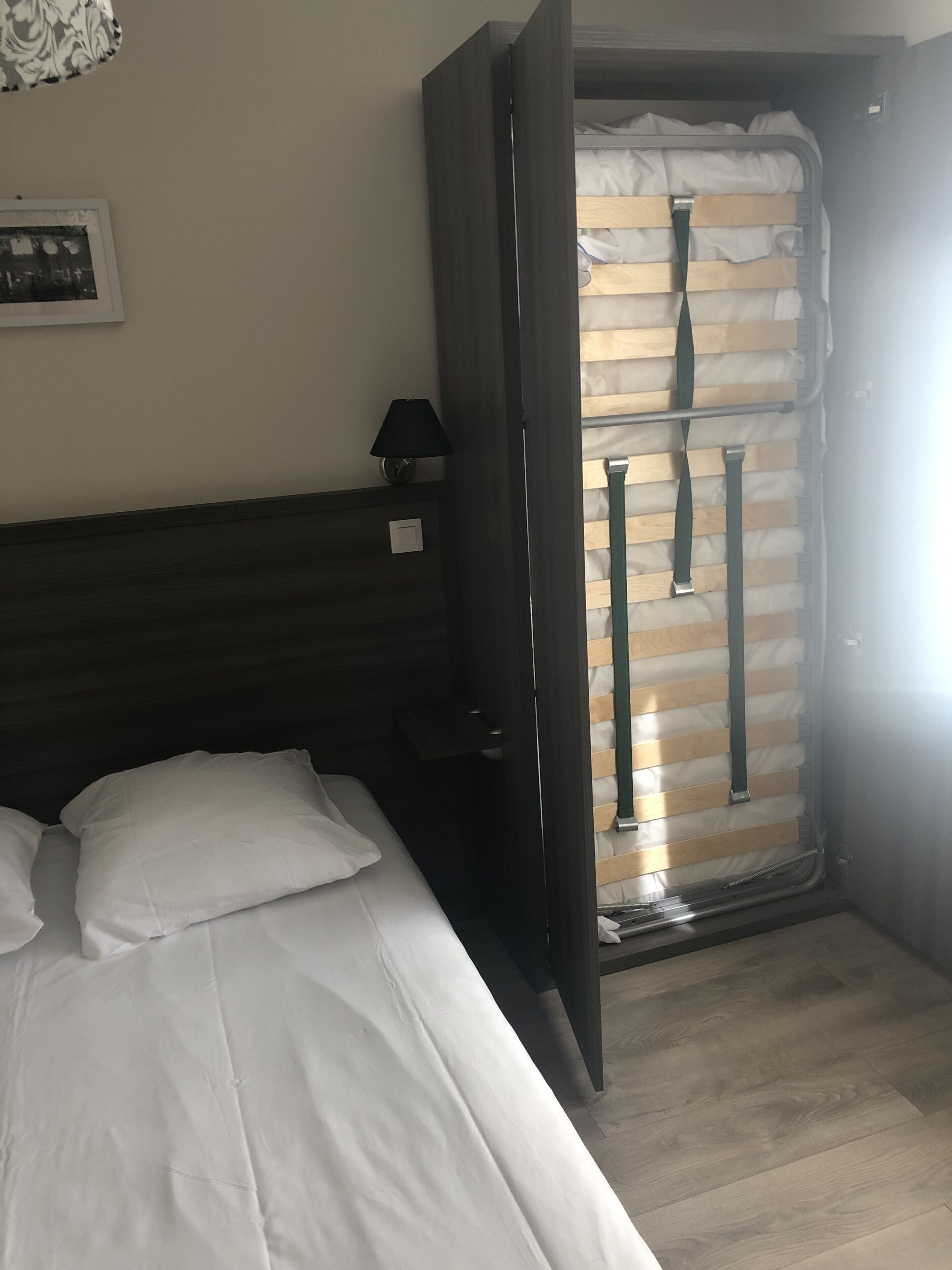 A hotel room with a bed, a nightstand, a lamp, and a view of a balcony with a railing.