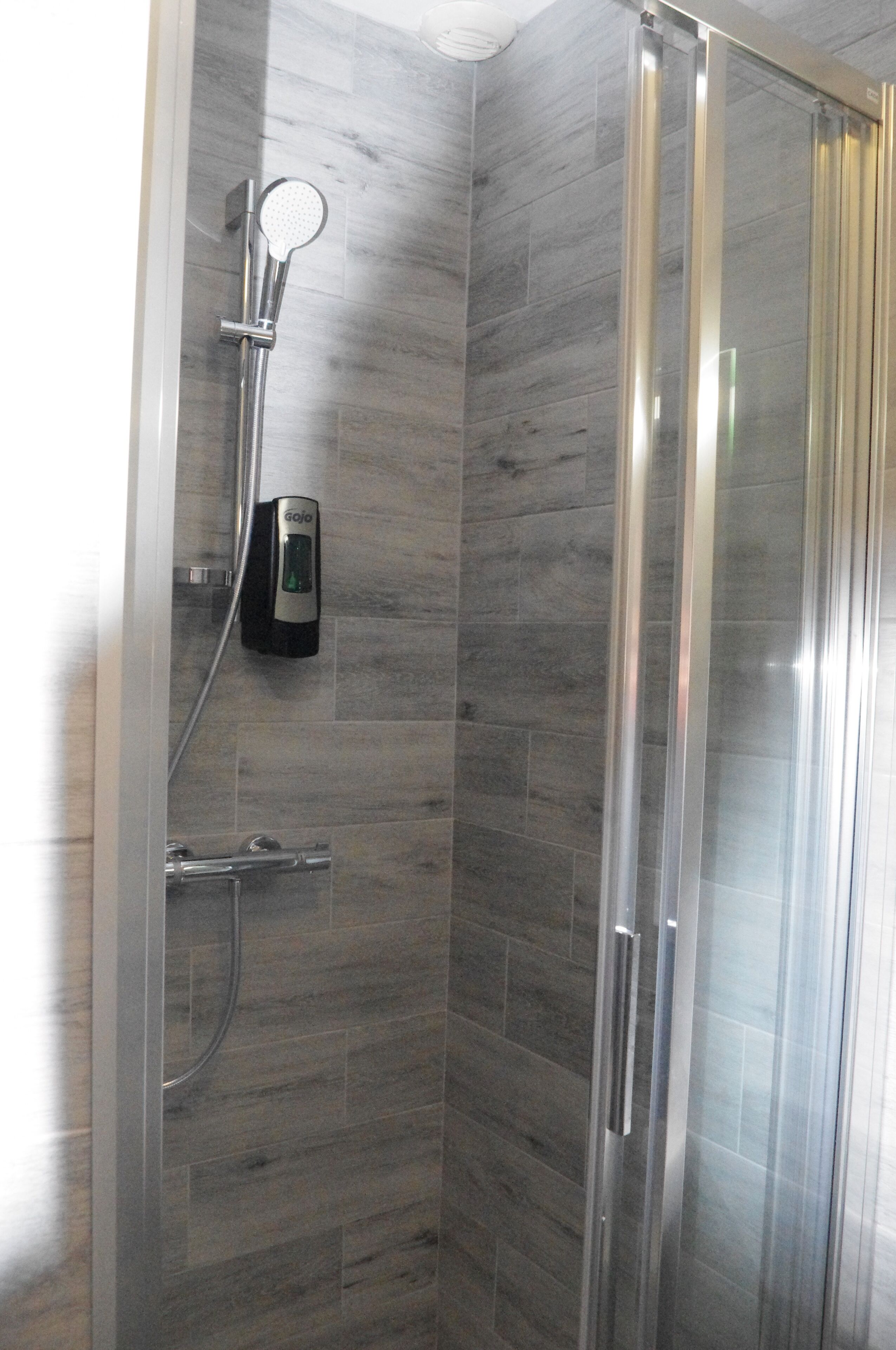 A glass-enclosed shower with a handheld showerhead and a wall-mounted control panel.