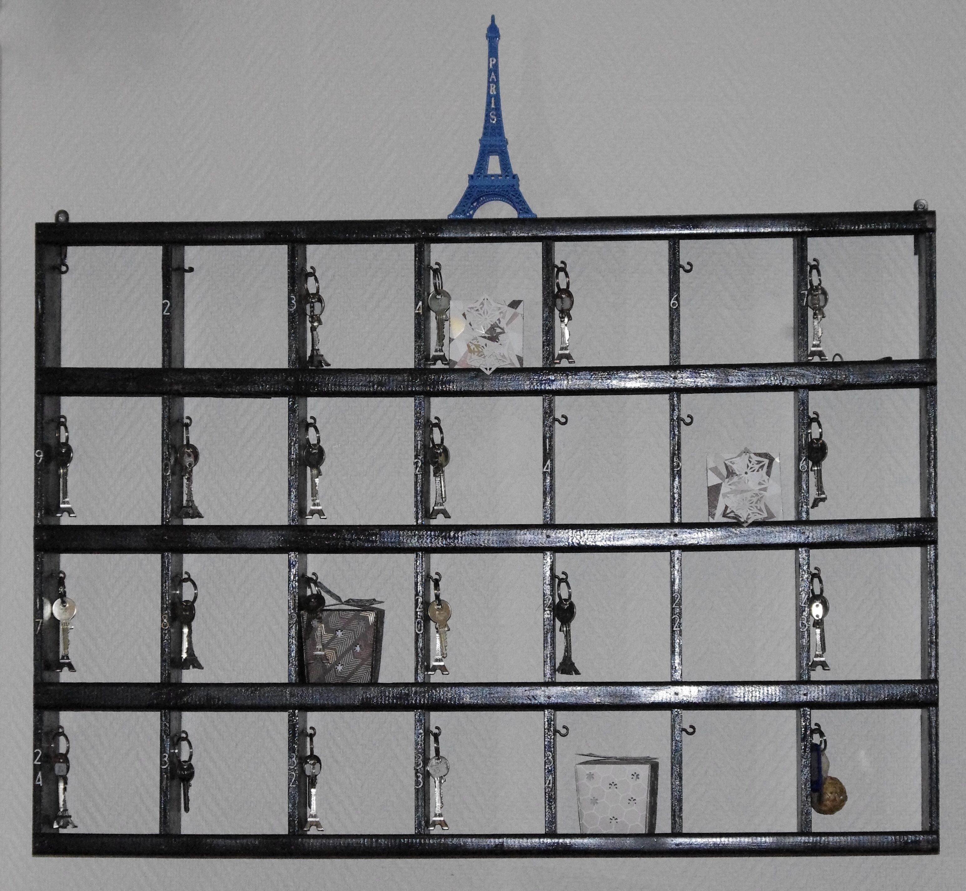 A metal rack with numbered slots holding various keys and a small Eiffel Tower model.