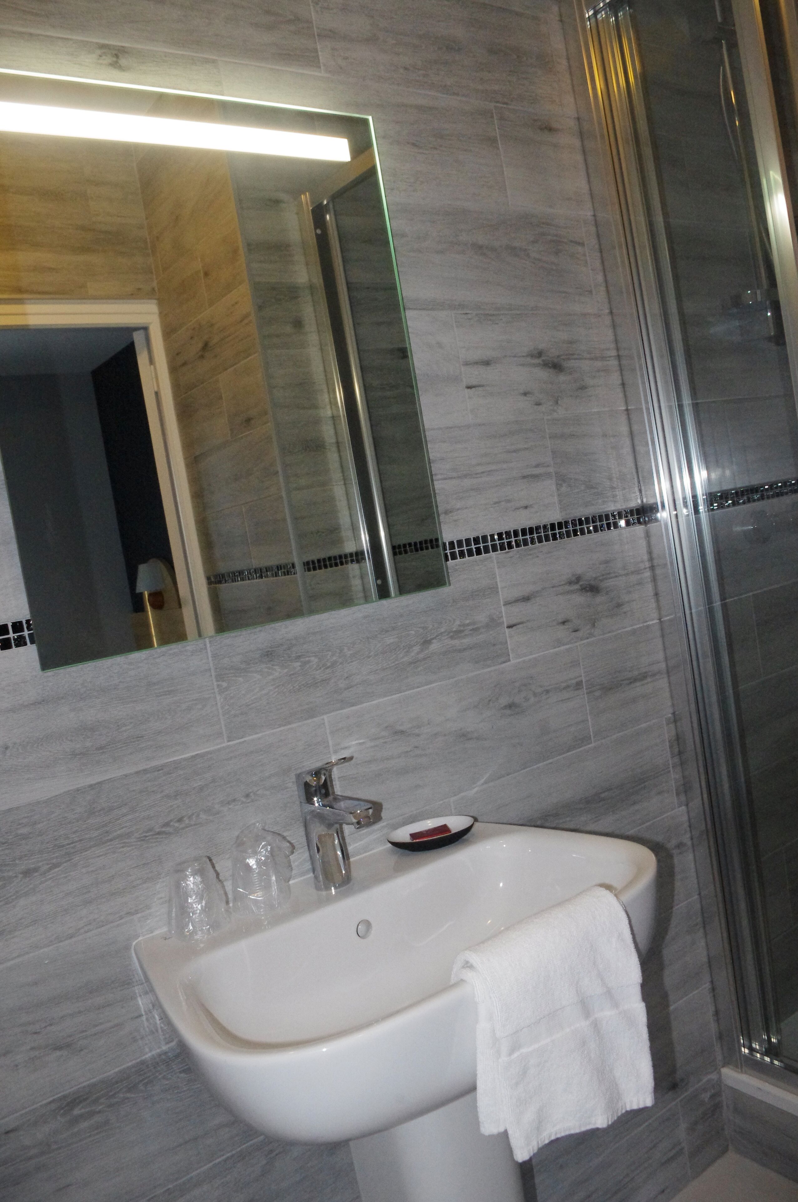 Un baño con lavamanos blanco, espejo y zona de ducha.