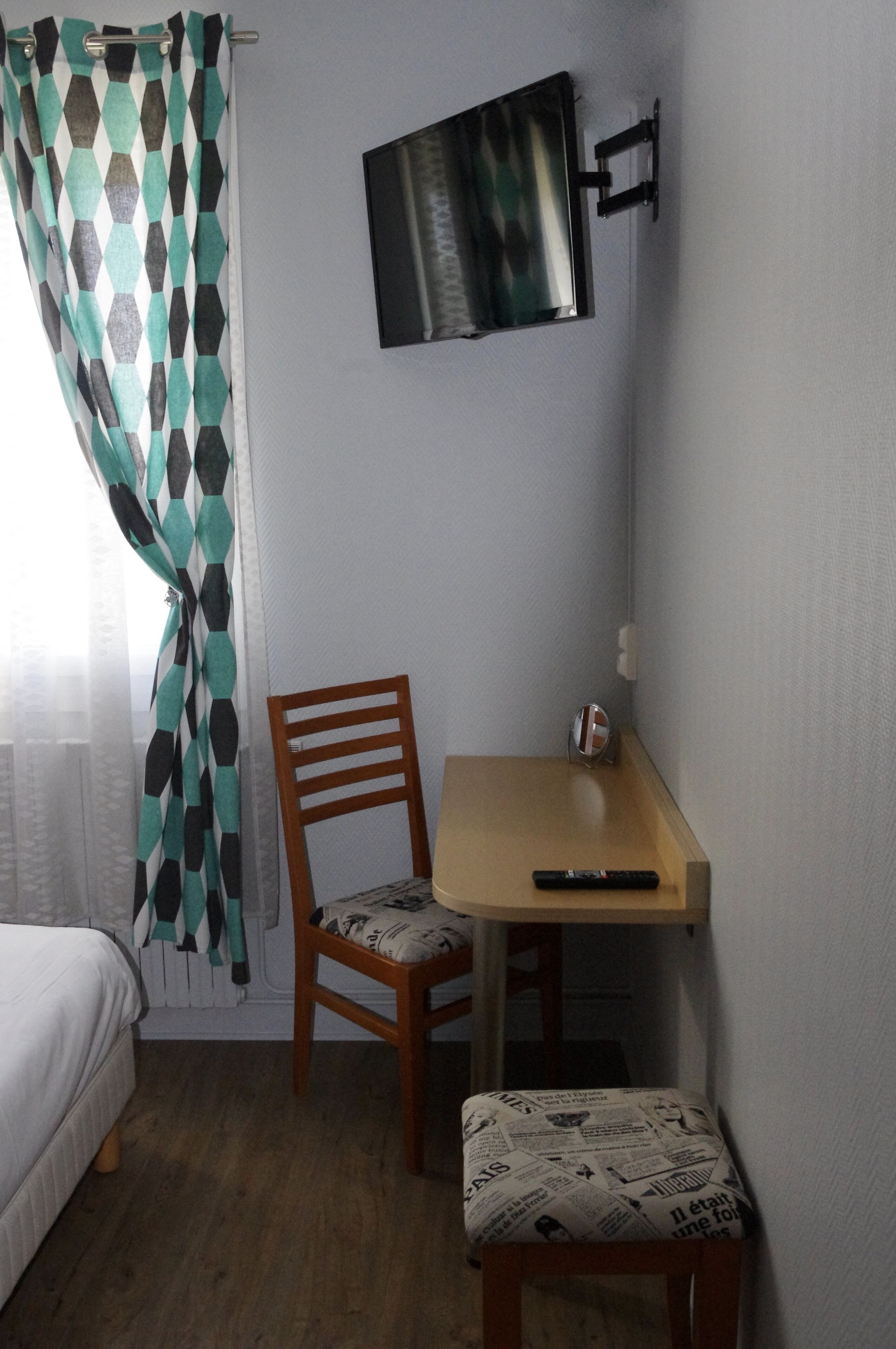 Una habitación pequeña con una cama, una silla de madera, una mesita y un televisor en la pared.