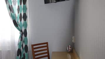 Una habitación pequeña con una cama, una silla de madera, una mesita y un televisor en la pared.