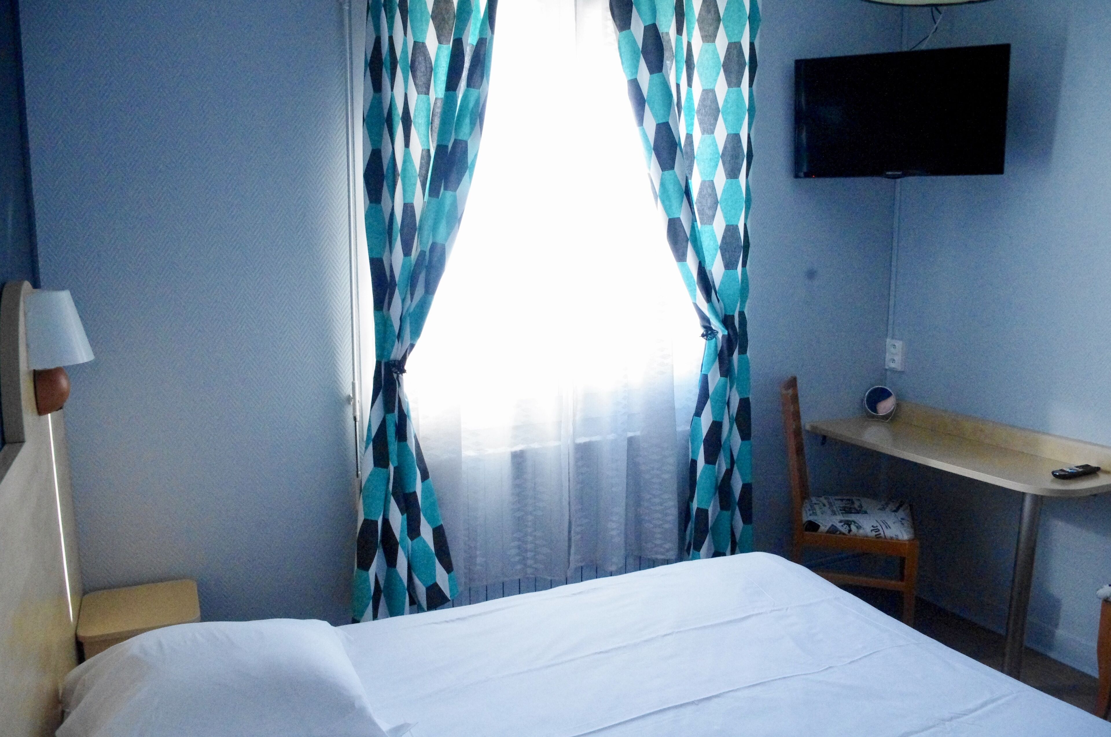 Una habitación de hotel con cama, escritorio, silla, televisor y cortinas.