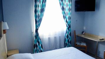 Una habitación de hotel con cama, escritorio, silla, televisor y cortinas.