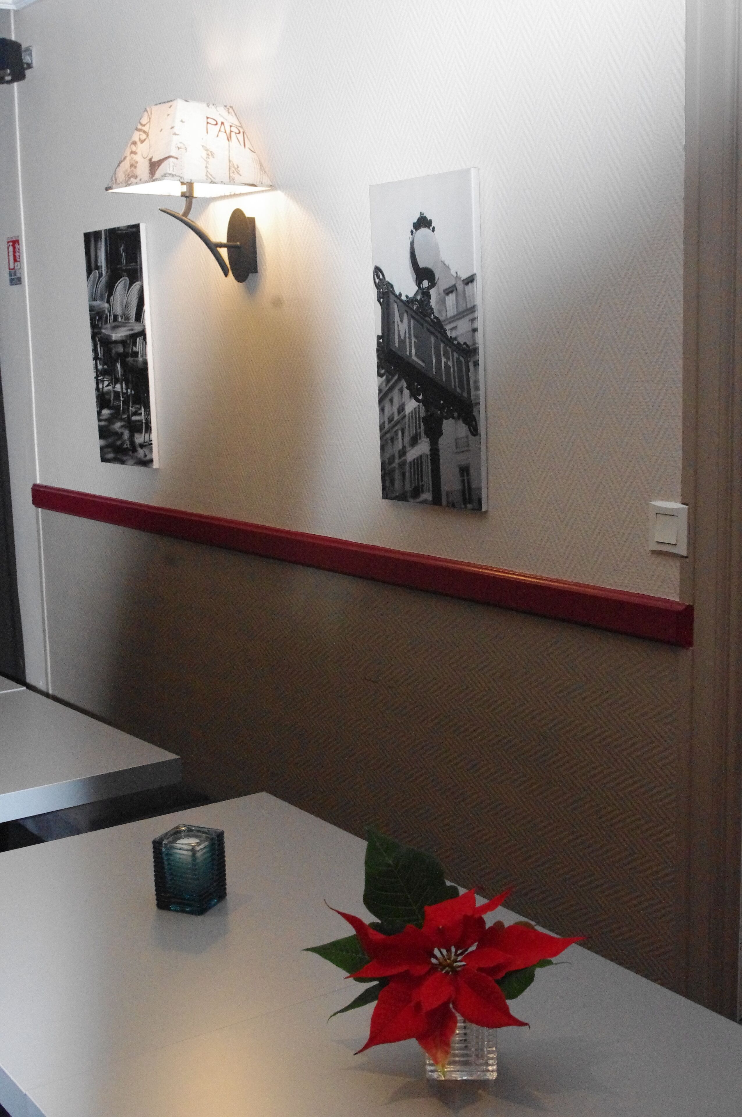 En hotellobby med en väggmonterad lampa, en röd hylla och ett litet bord med en vas med röda blommor.