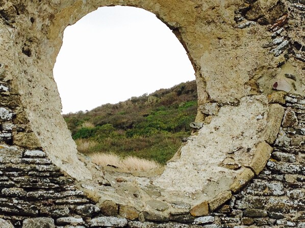 A circular stone opening with a view of a grassy hillside.
