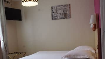 Un lit bien fait, recouvert d’une couette blanche, une table de chevet avec une lampe, une lampe suspendue à motifs en zigzag, une horloge murale et un téléviseur à écran plat fixé au mur.