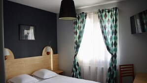 Una habitación de hotel con una cama, dos lámparas de noche, una silla, una mesa y un televisor en la pared.