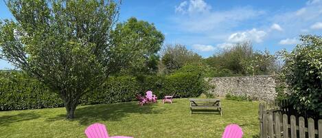 A grassy outdoor area with pink and yellow chairs, a small table, and a wooden bench.